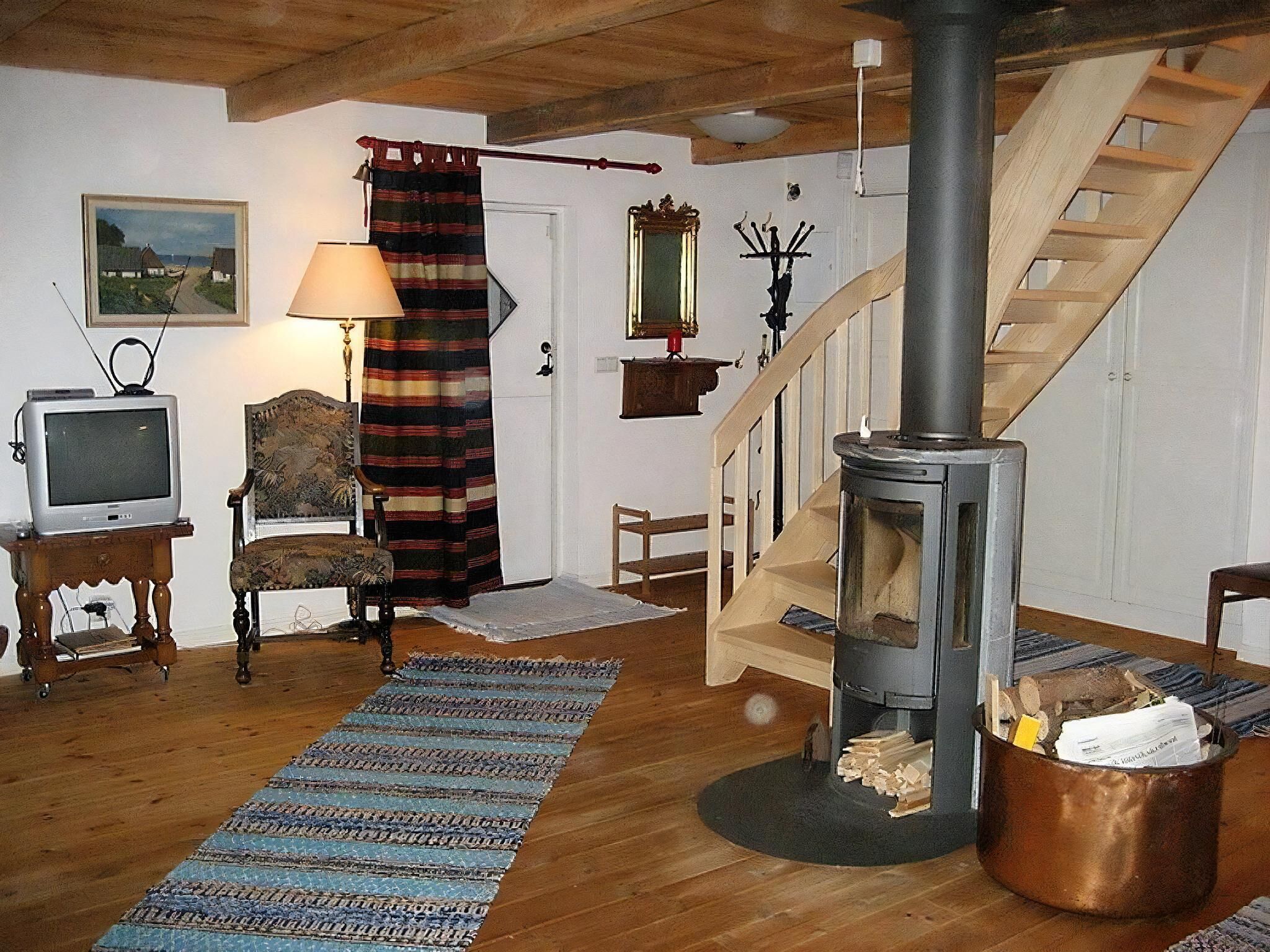 Uma sala de estar aconchegante com piso de madeira, televisão, uma poltrona, lareira e escada.