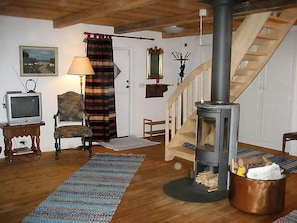 Ein gemütliches Wohnzimmer mit Holzboden, Fernseher, Sessel, Kamin und Treppe.