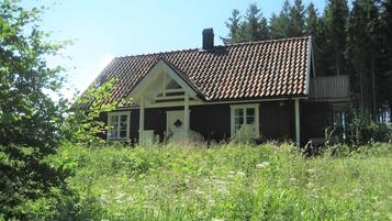 Et hus med et tegltag, omgivet af frodig vegetation og høje træer.