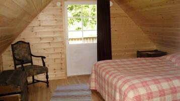 Et trægulvsrum med en seng, en stol og en dør, der fører udendørs.