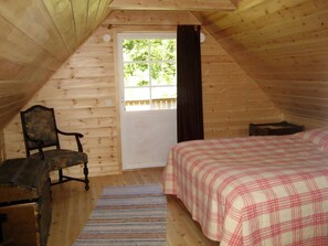 Ein Zimmer aus Holz mit einem Bett, einem Stuhl und einer Tür, die nach draußen führt.