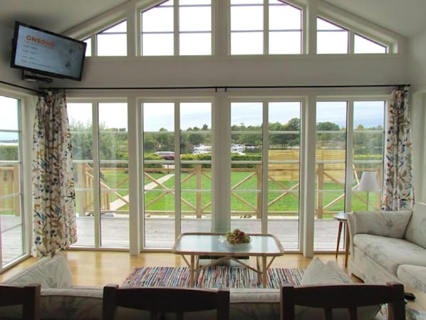 A spacious room with a large sliding glass door leading to an outdoor area, a flat-screen TV mounted on the wall, and a comfortable seating area with a sofa and chairs. - Panoramic sea-view from the house (Bräkne-Hoby)