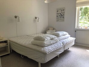 Une chambre à coucher comprenant un lit, deux lampes fixées au mur, un radiateur et une fenêtre donnant sur un espace verdoyant.