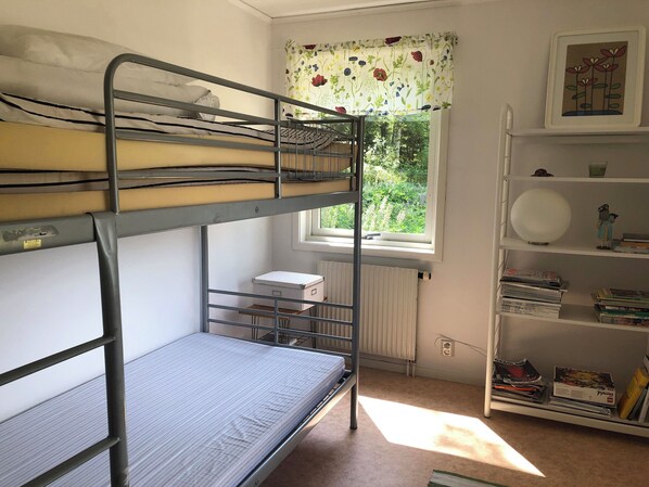 A bunk bed room with a radiator, a window with a floral curtain, and a bookshelf with books and decorative items. - Lovely house by the lake! Incl. rowing boat. (Aplared)