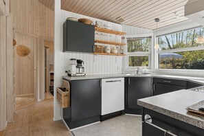 Eine moderne Küche mit Holzausstattung, einem Geschirrspüler und einem Fenster mit Blick ins Grüne.