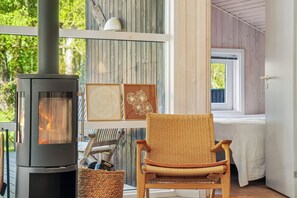 Ein Zimmer mit Kaminofen, Korbsessel und gerahmten Bildern.