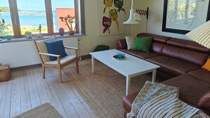 Een woonkamer met uitzicht op zee, een bruine leren bank, een witte salontafel en een houten stoel.