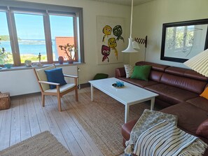 A living room with a view of the sea, a brown leather sofa, a white coffee table, and a wooden chair. - Sea view and calm near the shore in Thorøhuse (Assens)