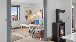 Een gezellige woonkamer met een open haard, een bank, een salontafel en een schilderij aan de muur.