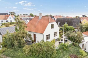 Ein Wohngebiet mit einem weißen Haus und einem roten Ziegeldach, umgeben von Grünflächen und angrenzenden Häusern im gleichen Baustil.