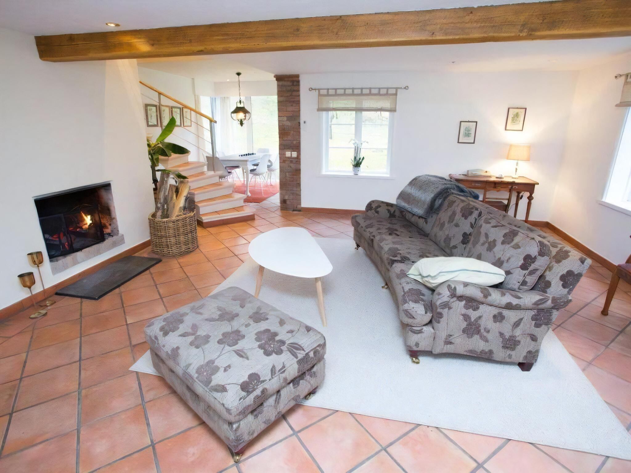 Ein Wohnzimmer mit Kamin, einer Couch, einem Hocker, einer Treppe und einem Essbereich.