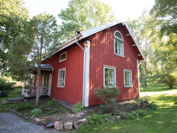 A red wooden house with a porch, surrounded by greenery and trees.