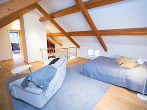 A loft bedroom with a high ceiling, wooden beams, a bed, a sofa, and a small table.