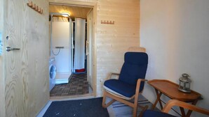 Un intérieur en bois avec une porte, une chaise, une petite table et un lave-linge à l’arrière-plan.
