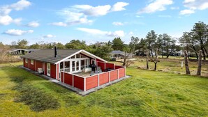 En röd stuga med en inglasad veranda, omgiven av en gräsklädd äng och träd.
