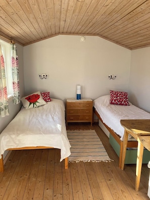 Ein Zimmer mit zwei Holzbetten, einem kleinen Holztisch, einem Nachttisch und einer Decke mit Holzbalken.