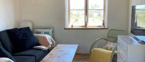 A cozy room with a wooden ceiling, a sofa, a table, a chair, a dresser, and a window.