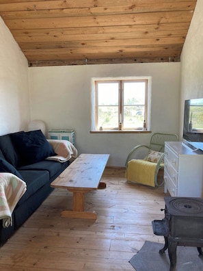 Ein gemütliches Zimmer mit Holzbalkendecke, einem Sofa, einem Tisch, einem Stuhl, einem Schminktisch und einem Fenster.