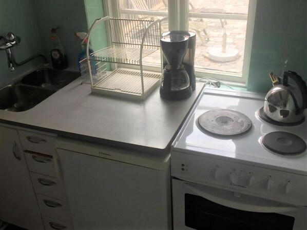 Una cocina con un lavamanos, un hervidor, una cafetera y una ventana con vistas al exterior.