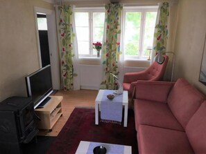 Ett vardagsrum med en tv, en röd soffa, ett vitt bord med en lampa och ett fönster med gardiner.