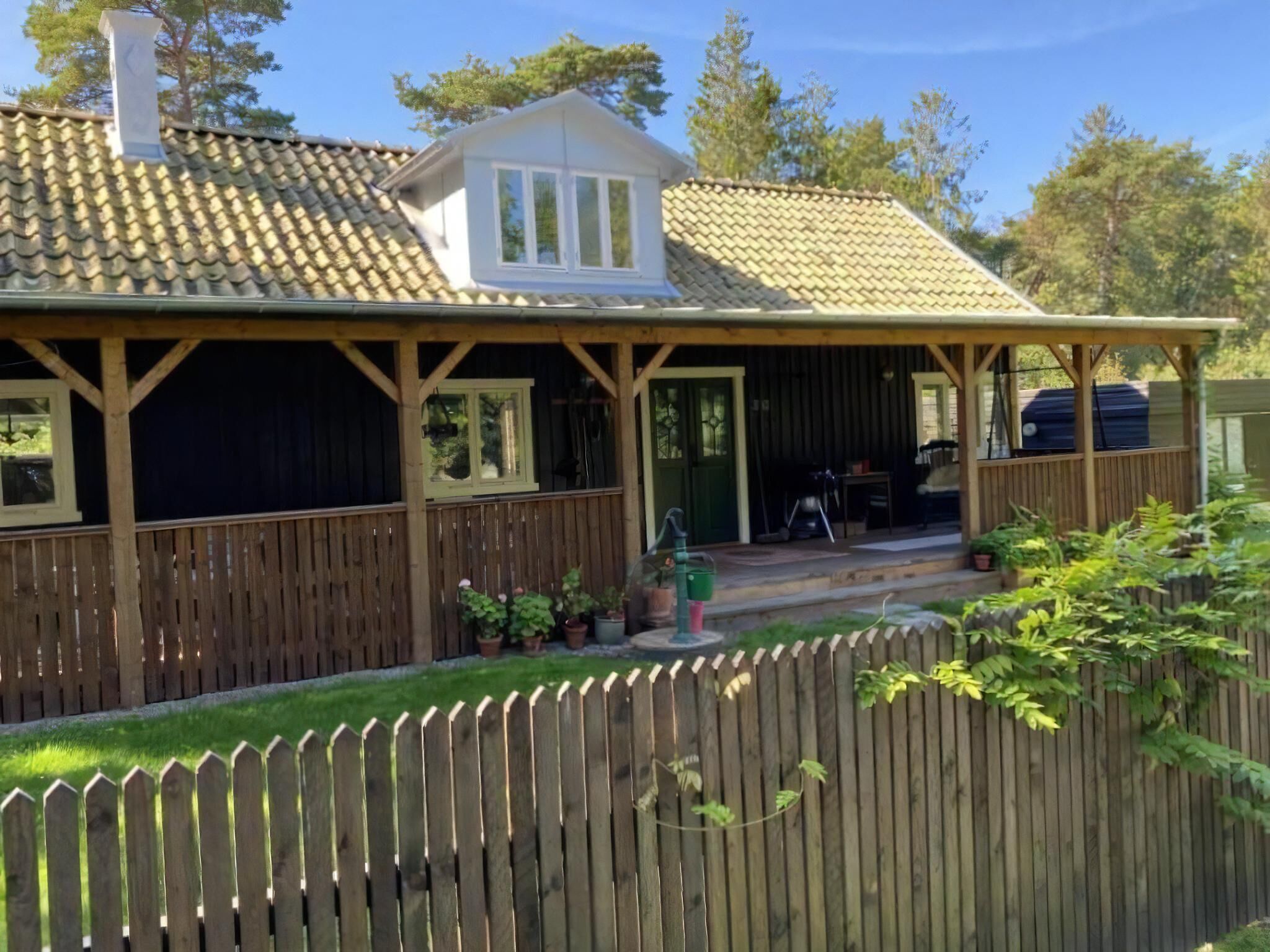 A wooden house with a tiled roof, a porch, and a fenced yard.