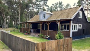 Ett trähus med en inglasad veranda, en inhägnad trädgård och en liten trädgård.