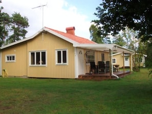 Ein eingeschossiges Haus mit rotem Dach, einer Veranda mit Stühlen und einem kleinen Garten.