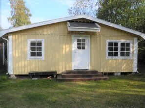 Ein eingeschossiges Holzhaus mit Satteldach, einer Haustür und je zwei Fenstern auf jeder Seite.