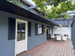 A covered patio with a wooden deck, a white door, and a seating area with white wicker furniture. - Marvelous views hygge in a cosy summer cottage (Asnæs)
