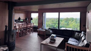 A spacious living area with a large window, a cozy seating area, a kitchen, and a wood-burning stove. - Marvelous views & hygge in a cosy summer cottage (Asnæs)