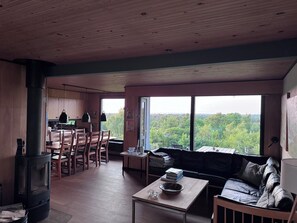 A spacious living area with a large window, a cozy seating area, a kitchen, and a wood-burning stove. - Marvelous views hygge in a cosy summer cottage (Asnæs)