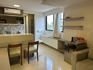 Eine moderne Küche mit integrierter Klimaanlage, einer Essecke mit zwei Stühlen, einem Sofa und einem Fenster mit Vorhängen.