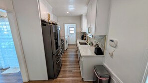 A narrow kitchen with white cabinets, a stainless steel refrigerator, a built-in oven, and a small trash bin. - Central 2BR 1 Bath House - 10 min to Beach, Sofi, & Restaurants (Inglewood)