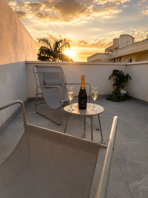 A rooftop terrace with a table, two chairs, a bottle of champagne, and two glasses.