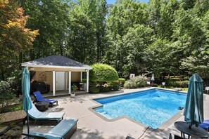A backyard with a swimming pool, lounge chairs, a covered patio, and a garden. - Luxury Retreat 20 Minutes from downtown- heated pool (Stockbridge)