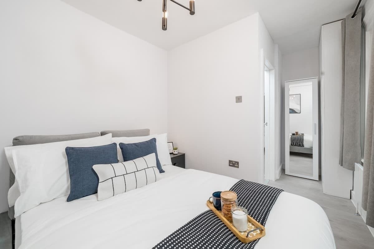 Ein modernes Hotelzimmer mit einem ordentlich bezogenen Bett, einem Nachttisch mit Lampe und Blick in das angrenzende Zimmer.