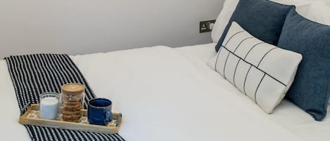 A bedroom with a bed, pillows, a tray with items, a chandelier, and two abstract wall art pieces.