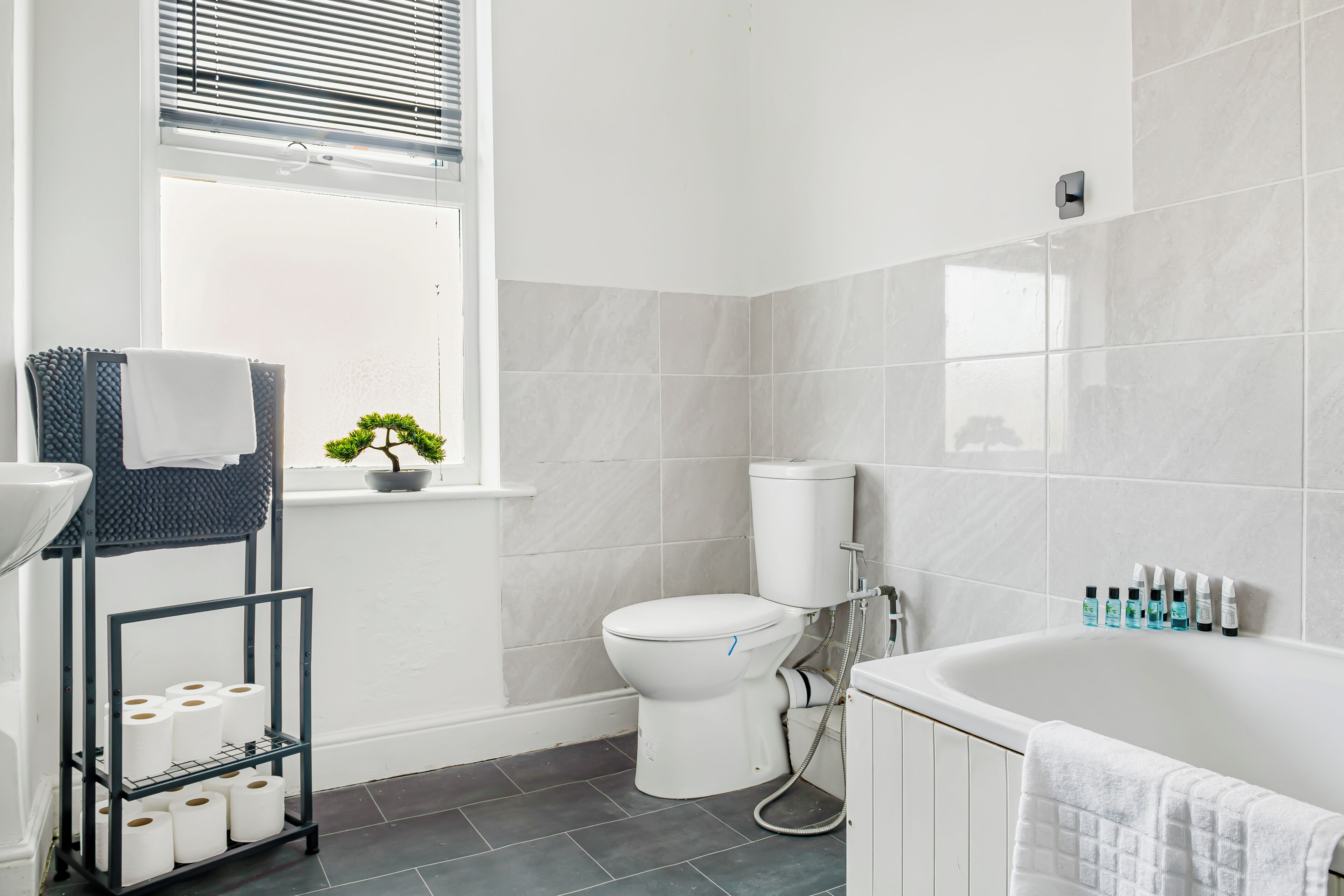 Un baño moderno con inodoro, lavabo, bañera y una ventana con persianas.