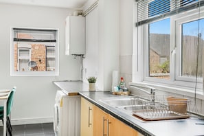 Eine moderne Küche mit eingebautem Geschirrspüler, einem Fenster mit Blick auf ein Backsteingebäude und einer Arbeitsplatte mit Geschirrgestell.