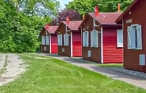 Eine Reihe roter Holzhütten mit weißen Fensterläden, ein Kiesweg und grünes Laub im Hintergrund.