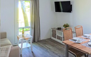 Ein Zimmer mit Esstisch, Stühlen, einem an der Wand montierten Fernseher und einem Fenster mit Vorhängen.