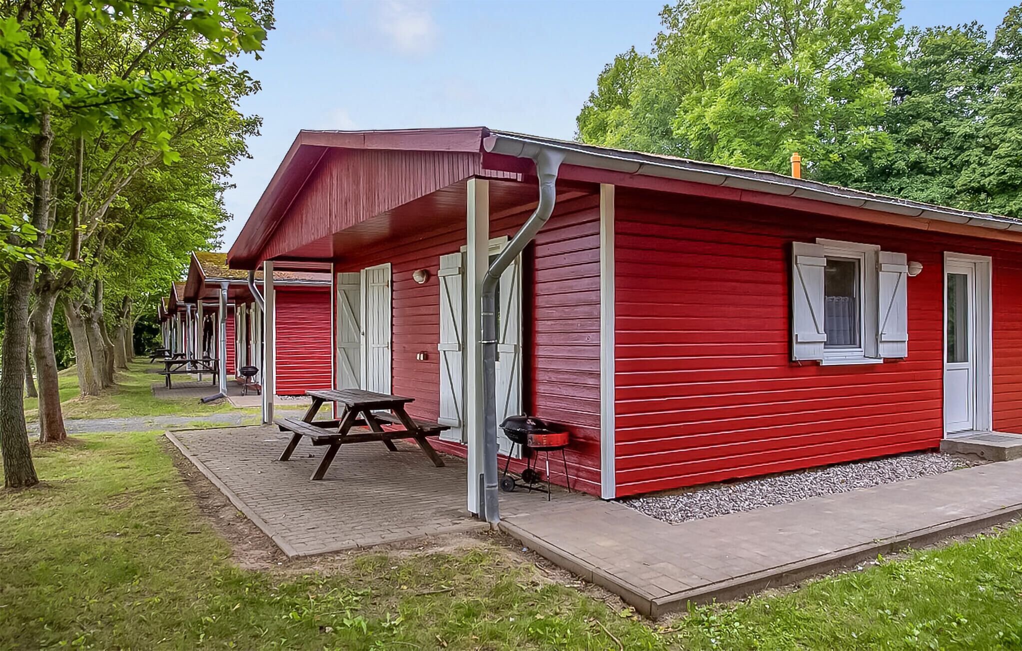 A red mobile home with a covered porch, a picnic table, and a grill.