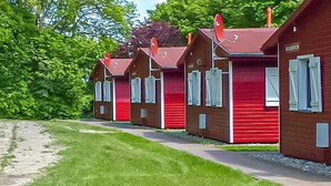 A row of red wooden cabins with white shutters, a gravel path, and green foliage in the background. - Nice home in Barth with house a panoramic view (Barth)
