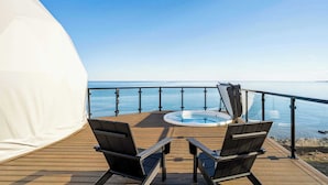 Un terrazza in legno con una vasca idromassaggio e due sedie, affacciata su uno specchio d'acqua.