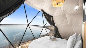 Ein Schlafzimmer mit großem Fenster, einem Bett, einem Nachttisch und einer Pendelleuchte.