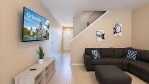 A living room with a large flat-screen TV, a sectional sofa, a console table, and a staircase. - Modern Townhome Minutes to Disney Pool (Kissimmee)