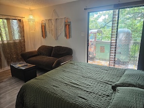 Een slaapkamer met een bed, een slaapbank, een macramé wanddecoratie en uitzicht op groen.