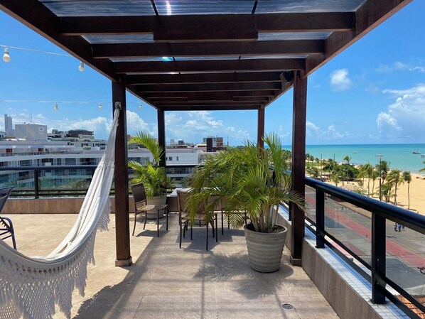 Ein Balkon mit einer Hängematte, Topfpflanzen und Blick auf Strand und Stadtbild.