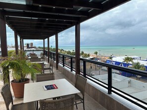 Ein überdachter Außenbereich mit Tischen und Stühlen mit Blick auf einen Strand und den Ozean.
