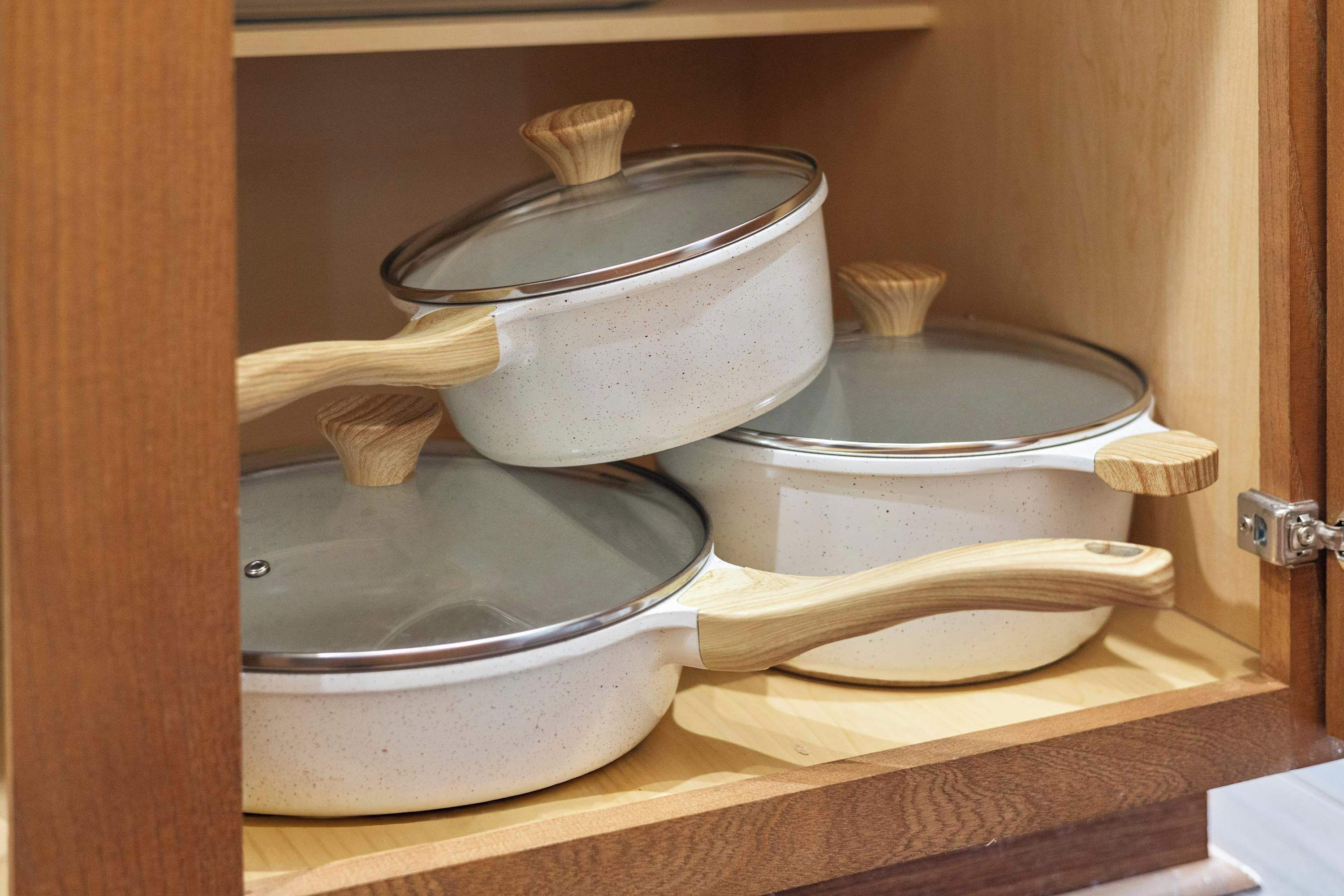 A wooden cabinet with three white ceramic pots with lids, each with a wooden handle.